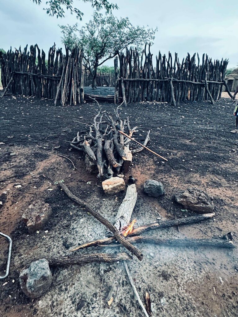 A Himba livestock kraal built from upright timber poles, with a fire burning in the foreground